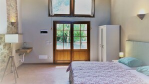 Ein Schlafzimmer mit Bett, Kleiderschrank, einem Fenster mit Vorhängen, einem Waschbecken und einer Steinwand.