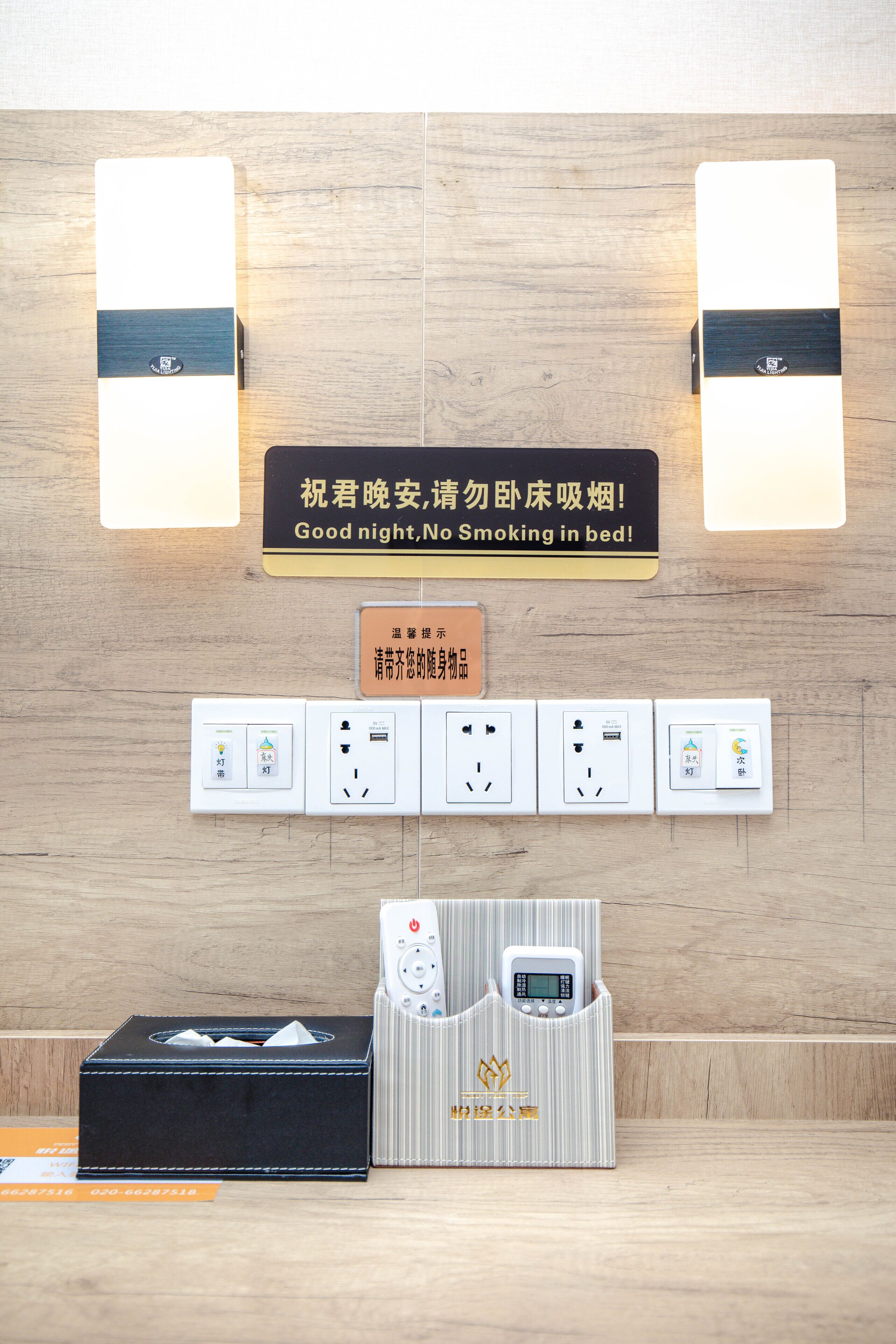 A hotel room with a wooden wall, a sign in Chinese, electrical outlets, a remote control, and a tissue box.