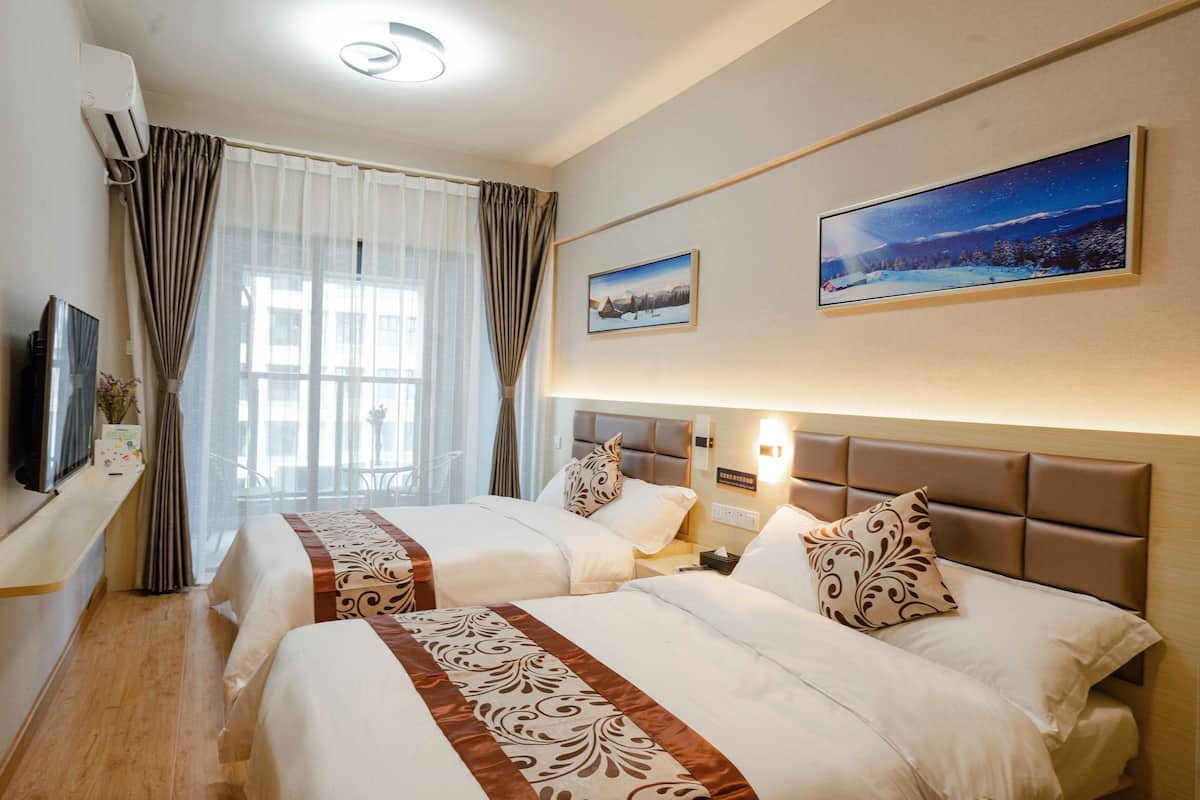 A hotel room with two beds, a flat-screen TV, a window with curtains, and two framed pictures on the wall.