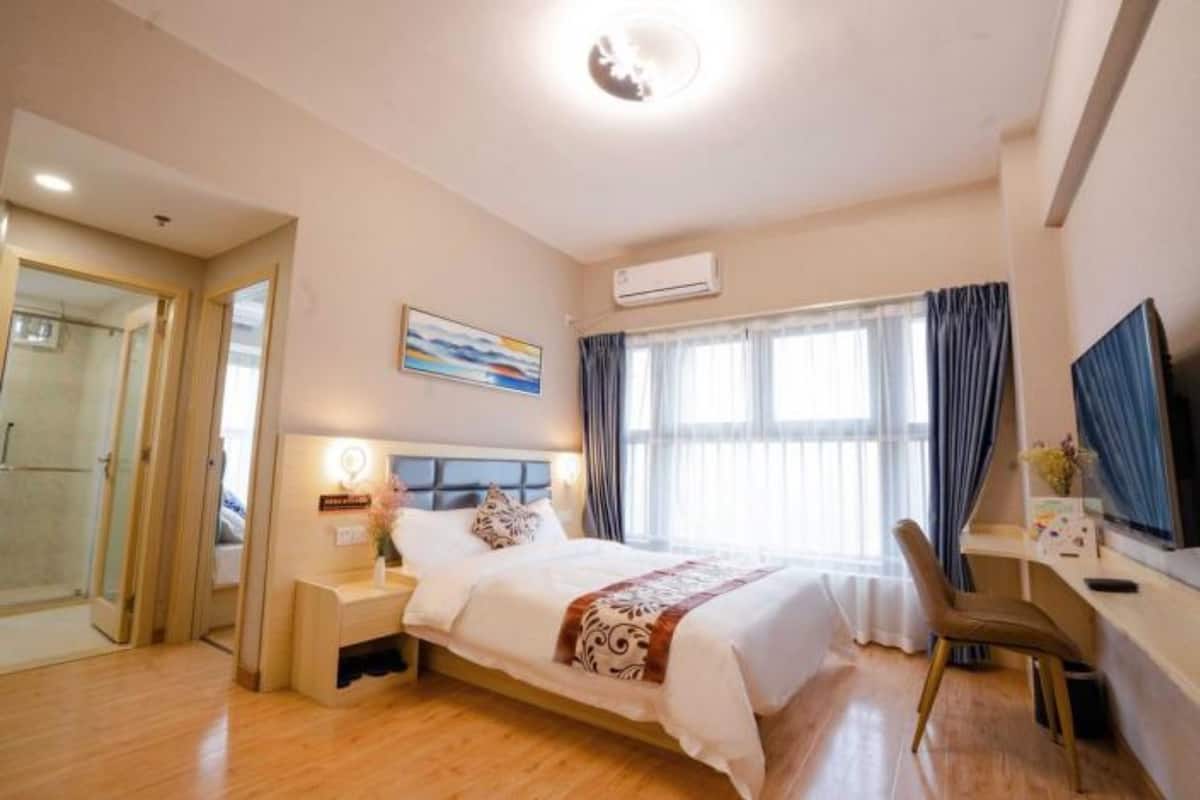 A hotel room with a bed, bedside table, chair, and a desk with a TV.