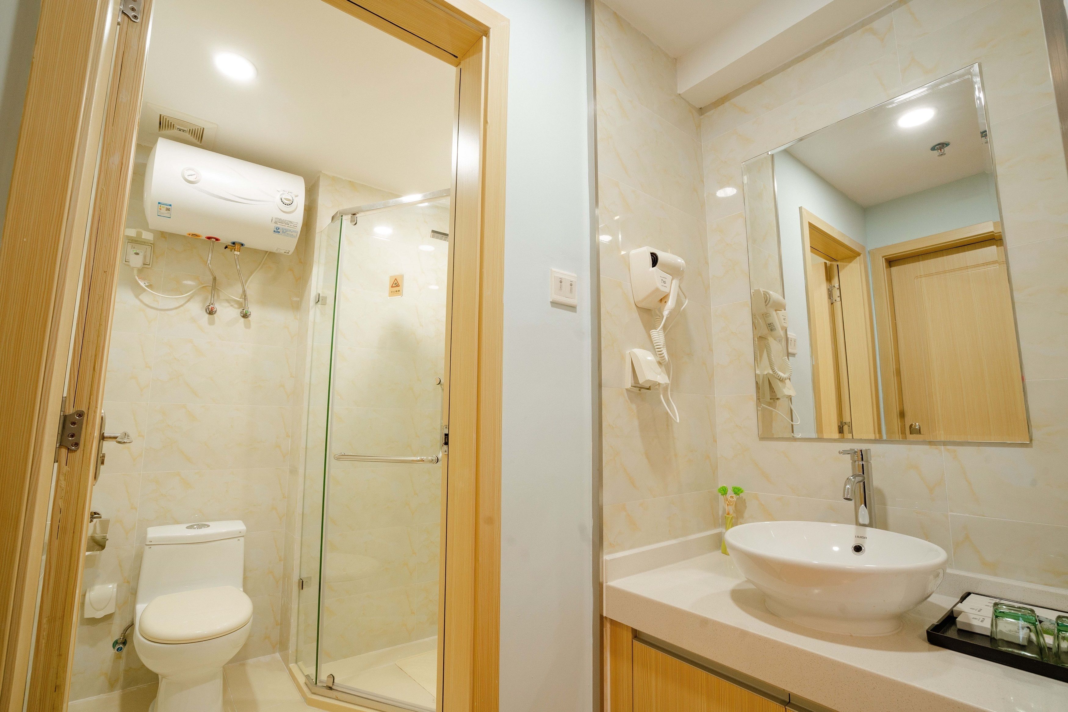 Un baño con inodoro, cabina de ducha de vidrio, lavabo con espejo y secador de pelo en la pared.