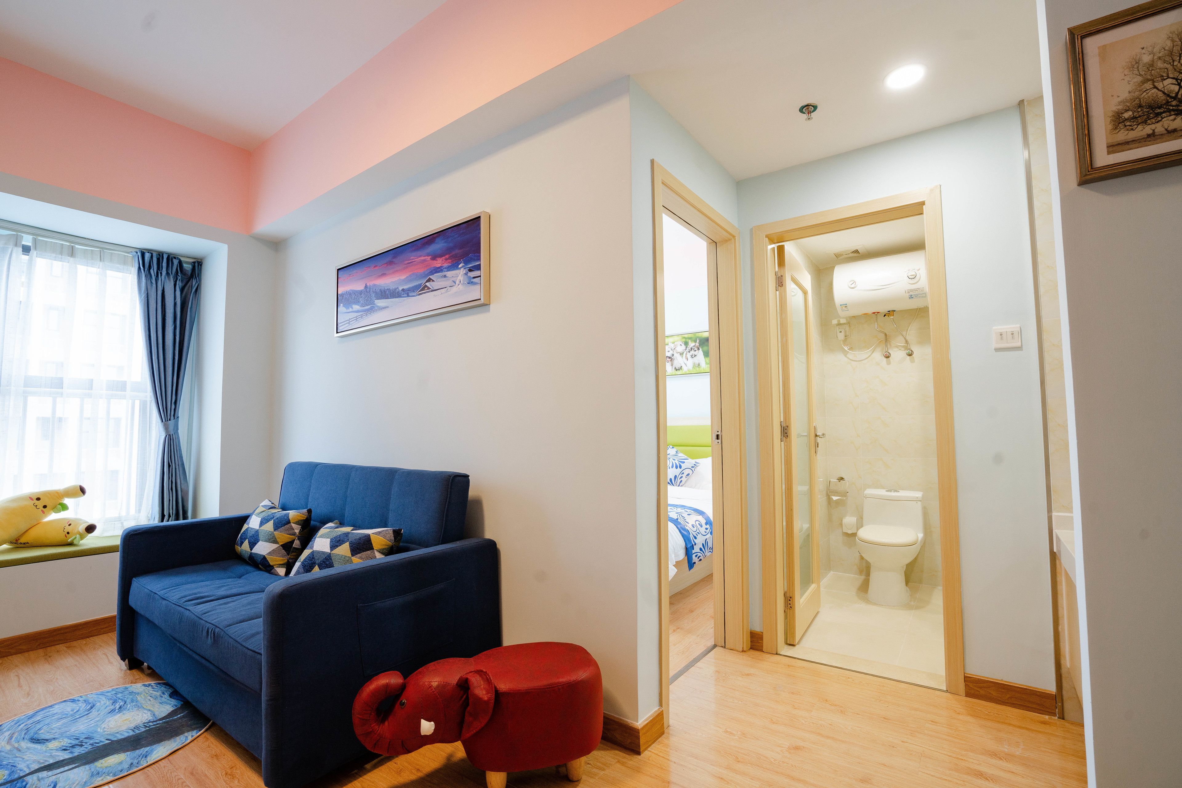 Una sala de estar con un sofá azul, un otoman rojo y una ventana con cortinas.