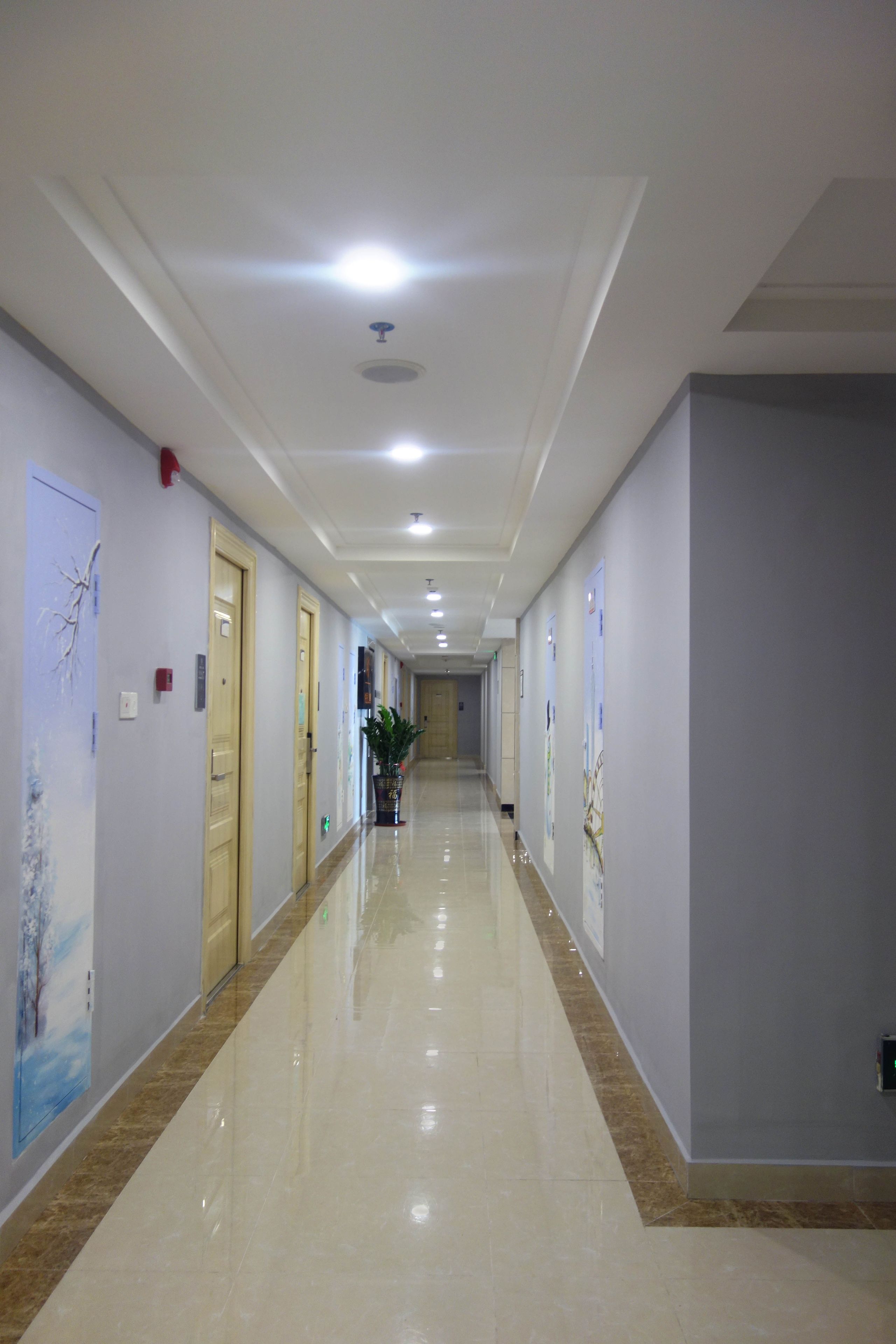 A long, well-lit hallway with doors on both sides, a polished floor, and a ceiling with recessed lighting.