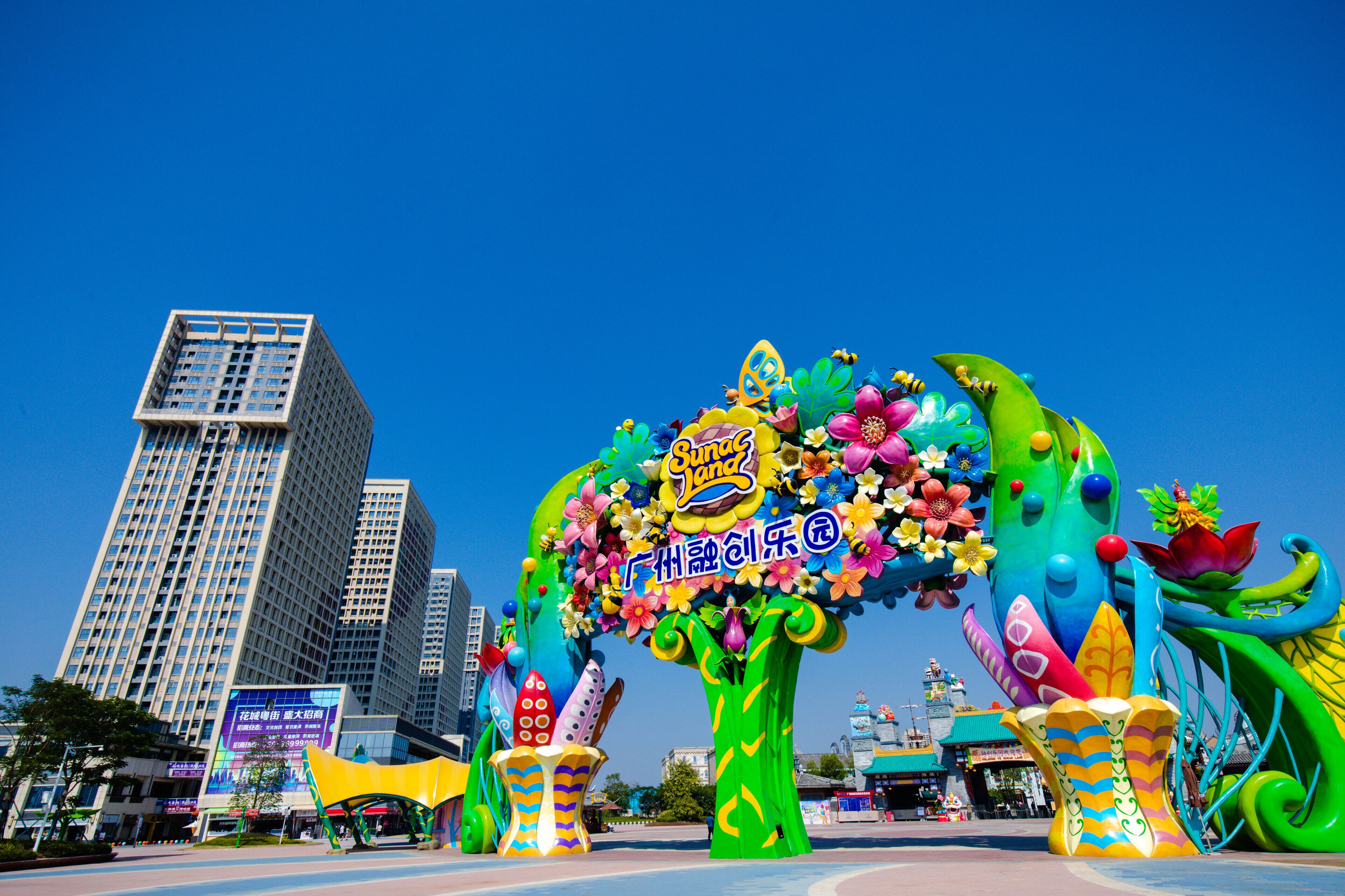 Un arco de colores con decoraciones florales y un letrero, frente a edificios altos.
