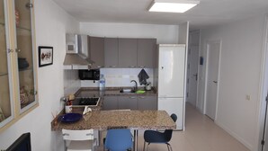 A compact kitchen with a microwave, sink, and a small refrigerator. There are two chairs and a table in the dining area. - Playa de las Américas Apartment (Arona)