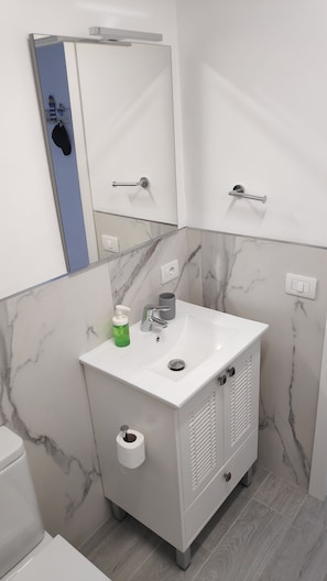 Ein modernes Badezimmer mit einem weißen Waschbecken, Marmorwänden, einem Spiegel und einer Toilette.