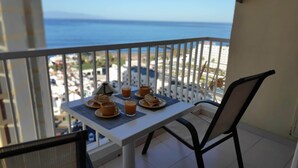 A balcony with a table set for breakfast, overlooking a beach and cityscape. - Playa de las Américas Apartment (Arona)