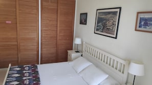 A hotel room with a bed, a nightstand, a lamp, a wooden wardrobe, and two framed pictures on the wall.