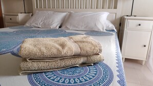 A neatly made bed with a patterned bedspread, two pillows, and a stack of folded towels. - Playa de las Américas Apartment (Arona)