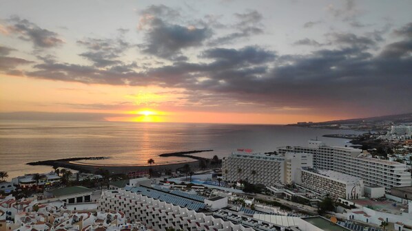 Eine Küstenlandschaft mit einem großen Hotel, einem Yachthafen und Blick auf den Sonnenuntergang über dem Meer.