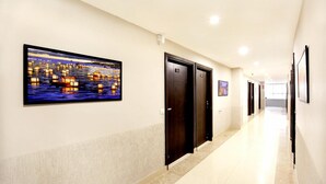 A hotel corridor with a large wall-mounted artwork depicting lanterns over water, three dark-colored doors, and a long, well-lit hallway. - Hotel Nanda (Ludhiana)