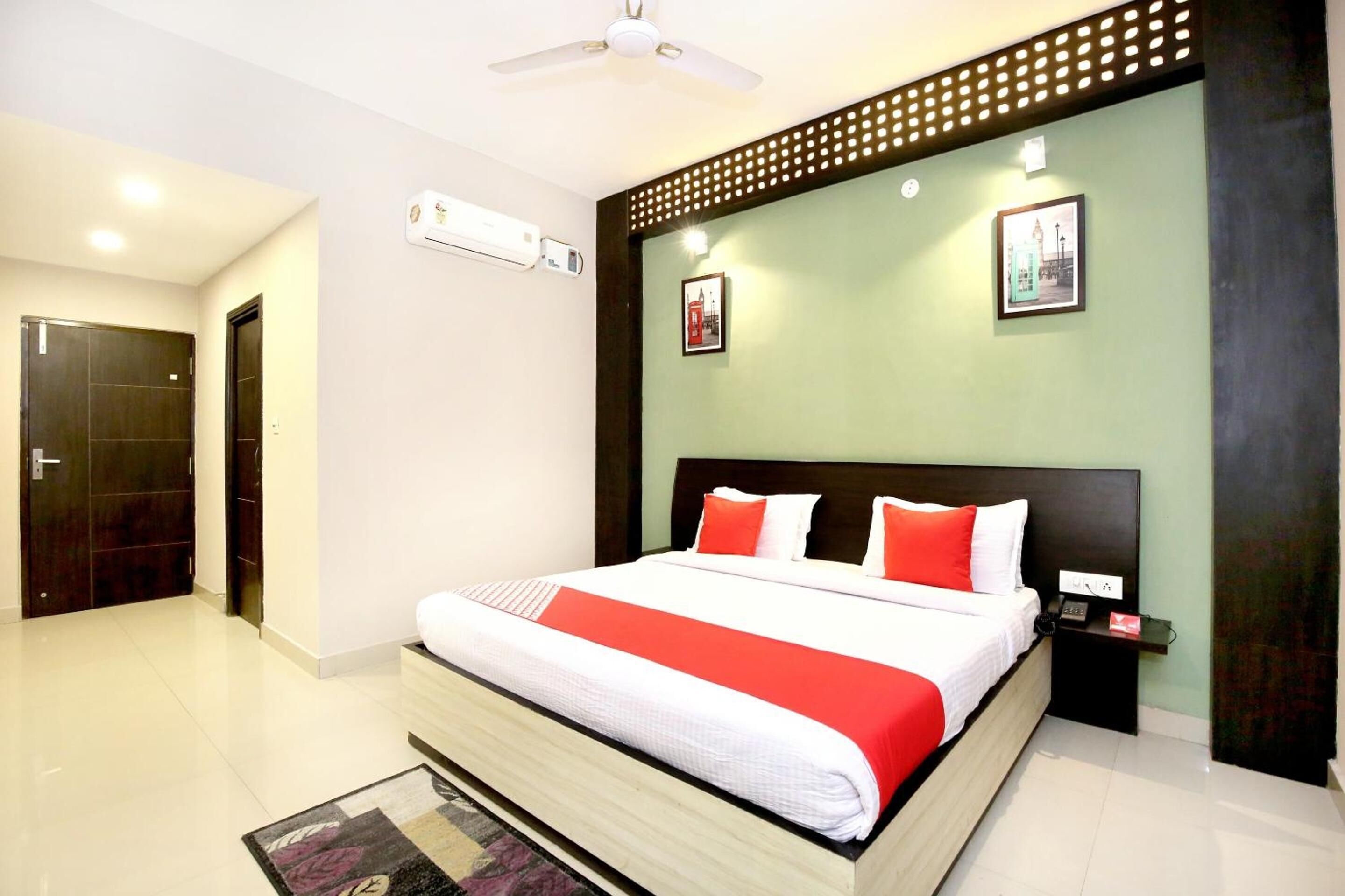 A modern hotel room with a large bed, a nightstand, a wall-mounted air conditioner, and a ceiling fan.