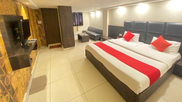 A hotel room with a large bed, a TV, a sofa, and a small table. - Hotel Nanda (Ludhiana)