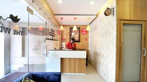 A hotel reception area with a wooden reception desk, a blue sofa with a floral cushion, and a wall-mounted clock. - Hotel Nanda (Ludhiana)
