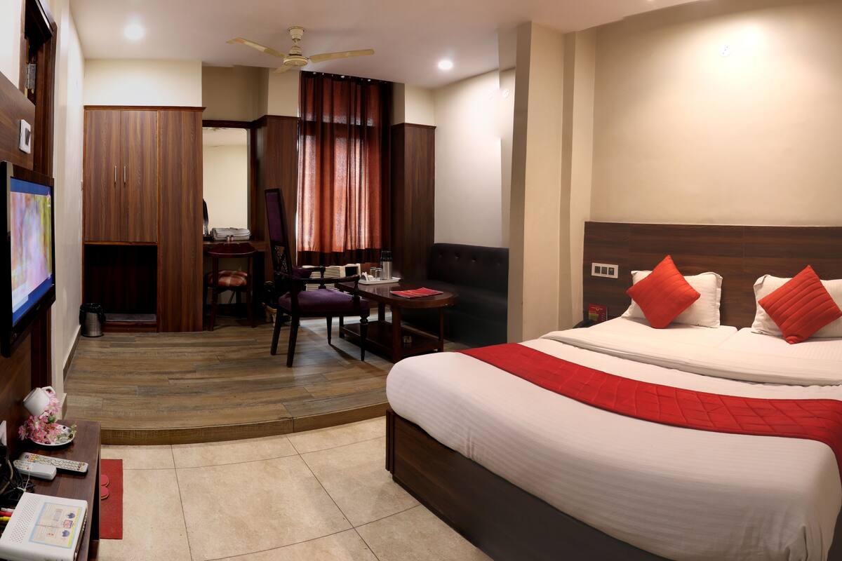 A hotel room with a large bed, a desk with a chair, a television, and a wardrobe.