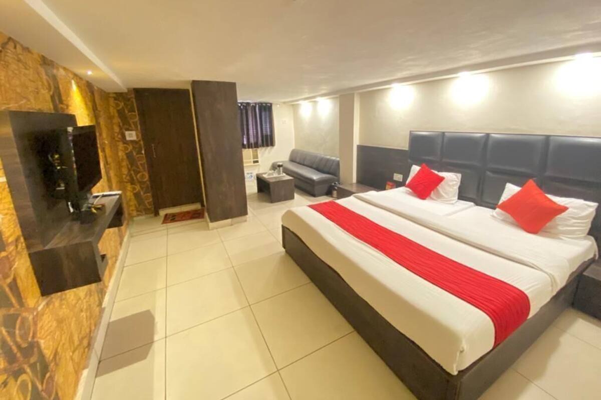 A hotel room with a large bed, a TV, a sofa, and a small table.