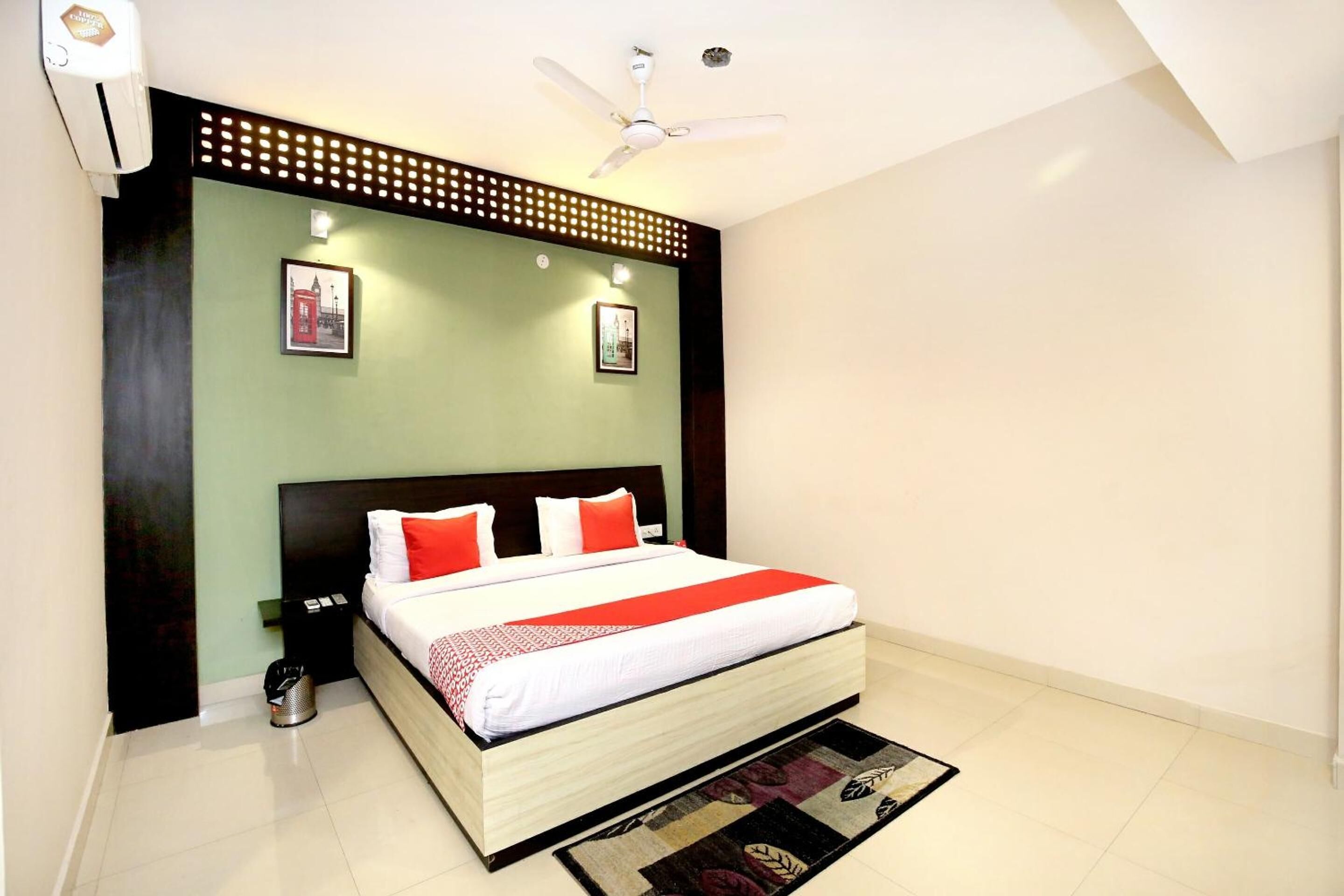 A bedroom with a bed, a ceiling fan, a wall-mounted air conditioner, and two framed pictures.