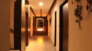 A hallway with a wooden door at the end, a wall-mounted light fixture, and a decorative metal plant on the right wall. - Hotel Nanda (Ludhiana)