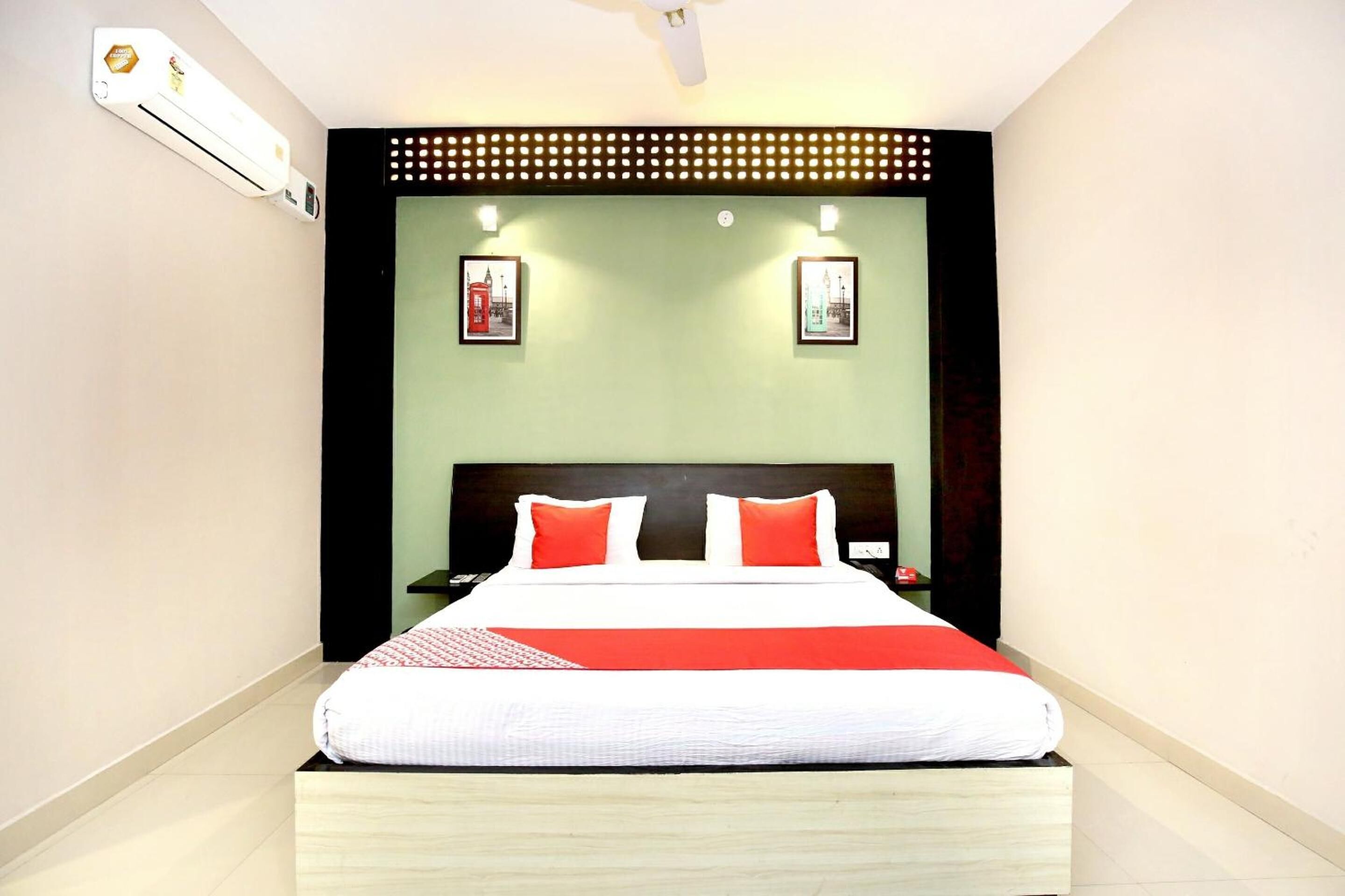 Una cama bien tendida con una colcha roja y blanca, un cabecero negro y dos mesitas de noche fijadas a la pared con lámparas rojas.