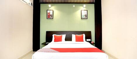 Un lit bien fait, recouvert d’une couvre-lit rouge et blanche, avec une tête de lit noire et deux tables de chevet fixées au mur, sur lesquelles sont posées des lampes rouges.