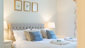 Un lit bien fait, avec des oreillers à rayures blanches et bleues, une tête de lit capitonnée et une table de chevet avec une lampe.