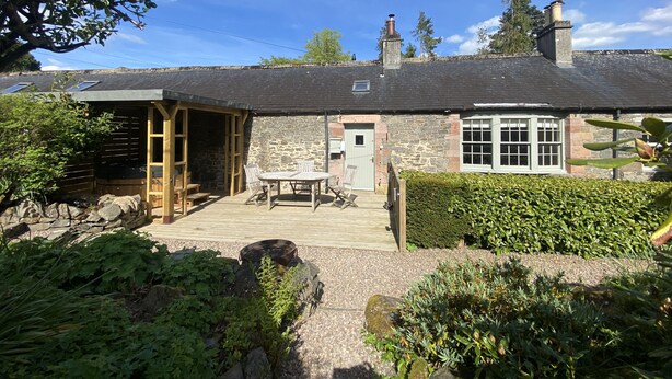 Une petite maison en pierre avec un porche en bois, une petite table et une chaise.