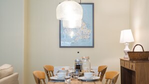 Une table à manger avec des chaises, un luminaire suspendu, une carte encadrée au mur et une lampe sur une table d’appoint.
