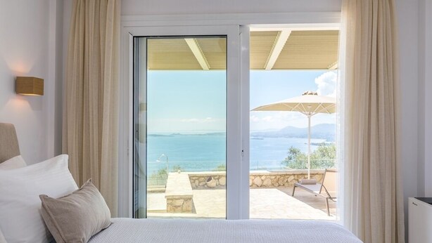 Un dormitorio con una cama grande, vistas al mar y un balcón con mobiliario exterior.