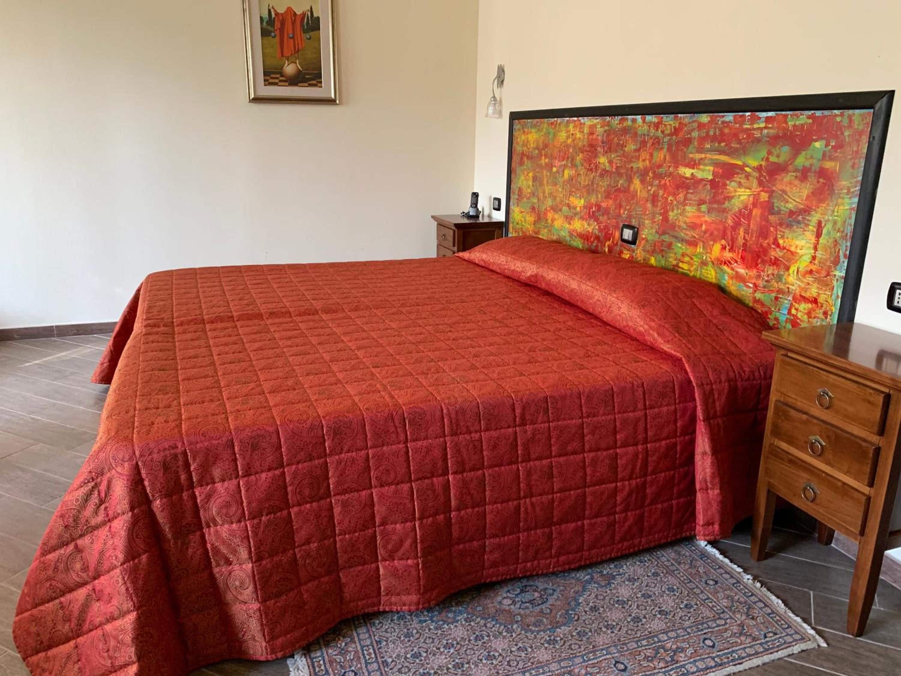 A bedroom with a large bed, a nightstand, a rug, and a colorful abstract painting on the wall.