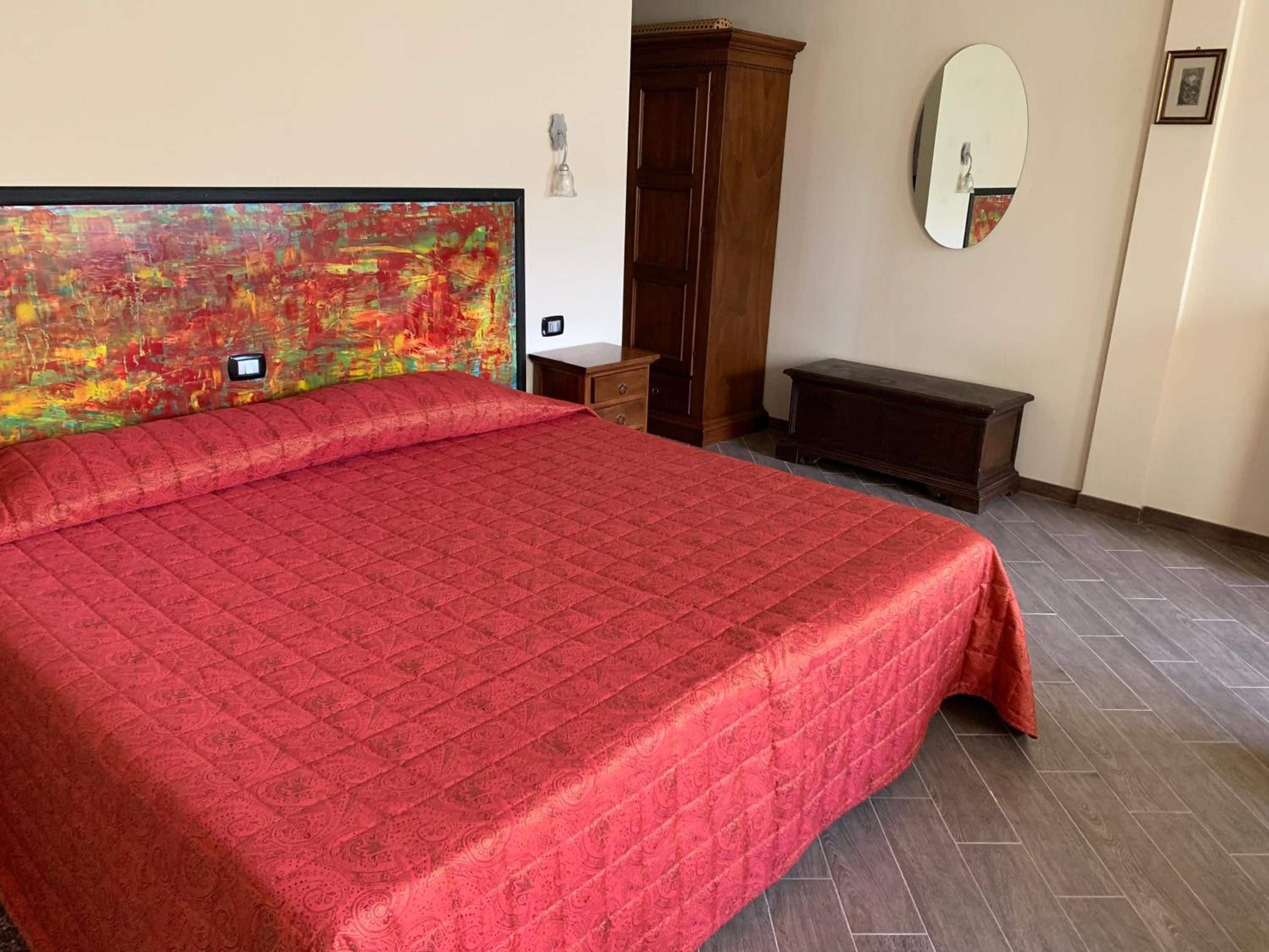 Ein Schlafzimmer mit einem großen Bett, einem Holzschrank, einer Bank und einem wandmontierten Spiegel.