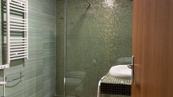 Ein Badezimmer mit grünen Fliesen, einem weißen Waschbecken, einer weißen Toilette und einem Bidet.