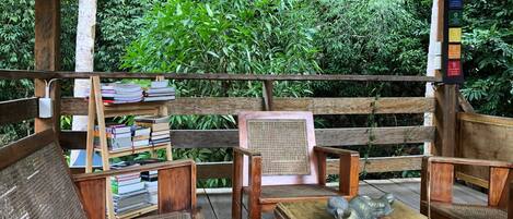 Een houten terras met een bank, tafel en stoel, omgeven door weelderige groene beplanting.