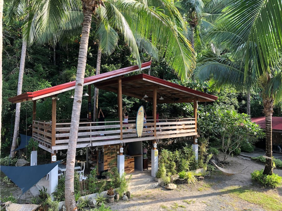 Une structure en bois surmontée d’un toit rouge, entourée d’une végétation luxuriante et de palmiers.