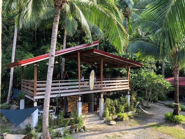 A wooden structure with a red roof, surrounded by lush greenery and palm trees.