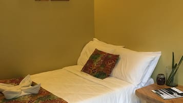 A neatly made bed with a floral bedspread, a wooden nightstand with a magazine, and a wall with multiple paintings.