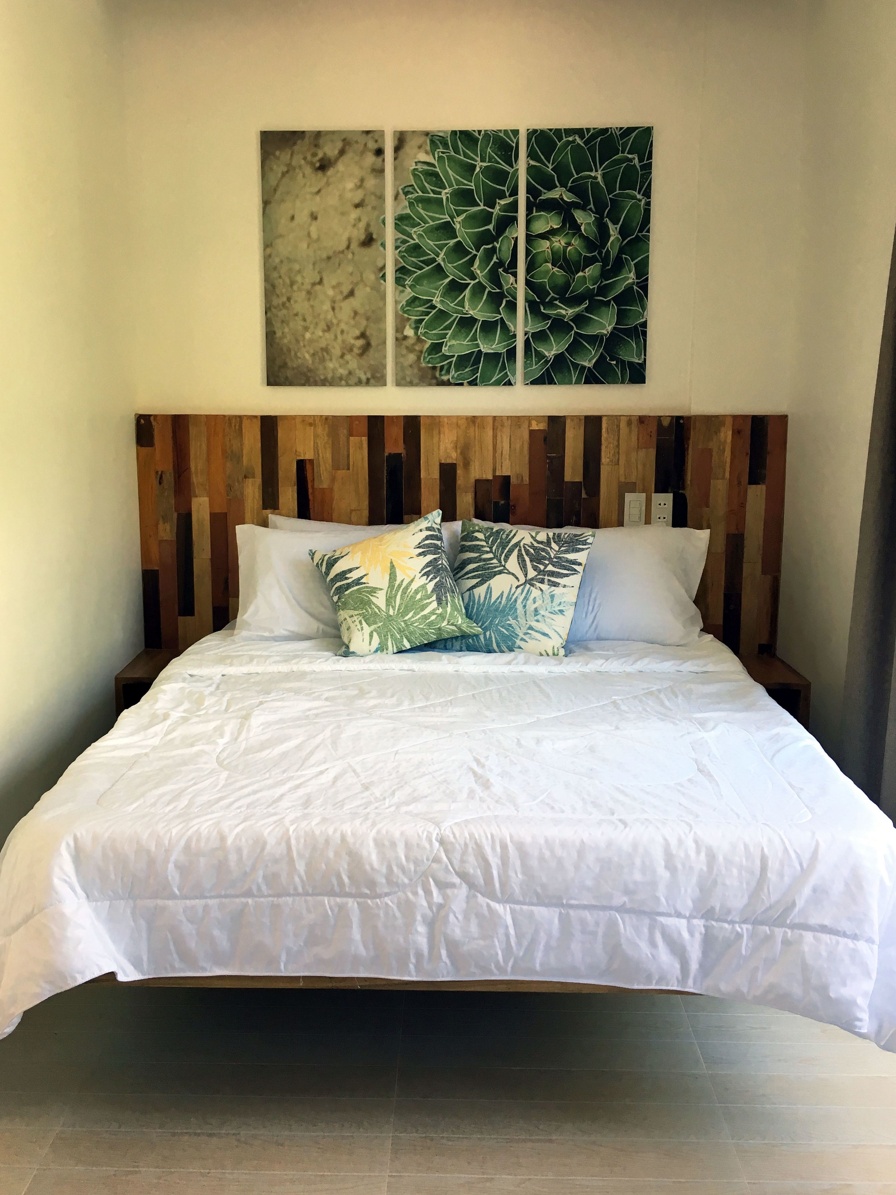 A bed with white bedding, a wooden headboard, and tropical-themed pillows.