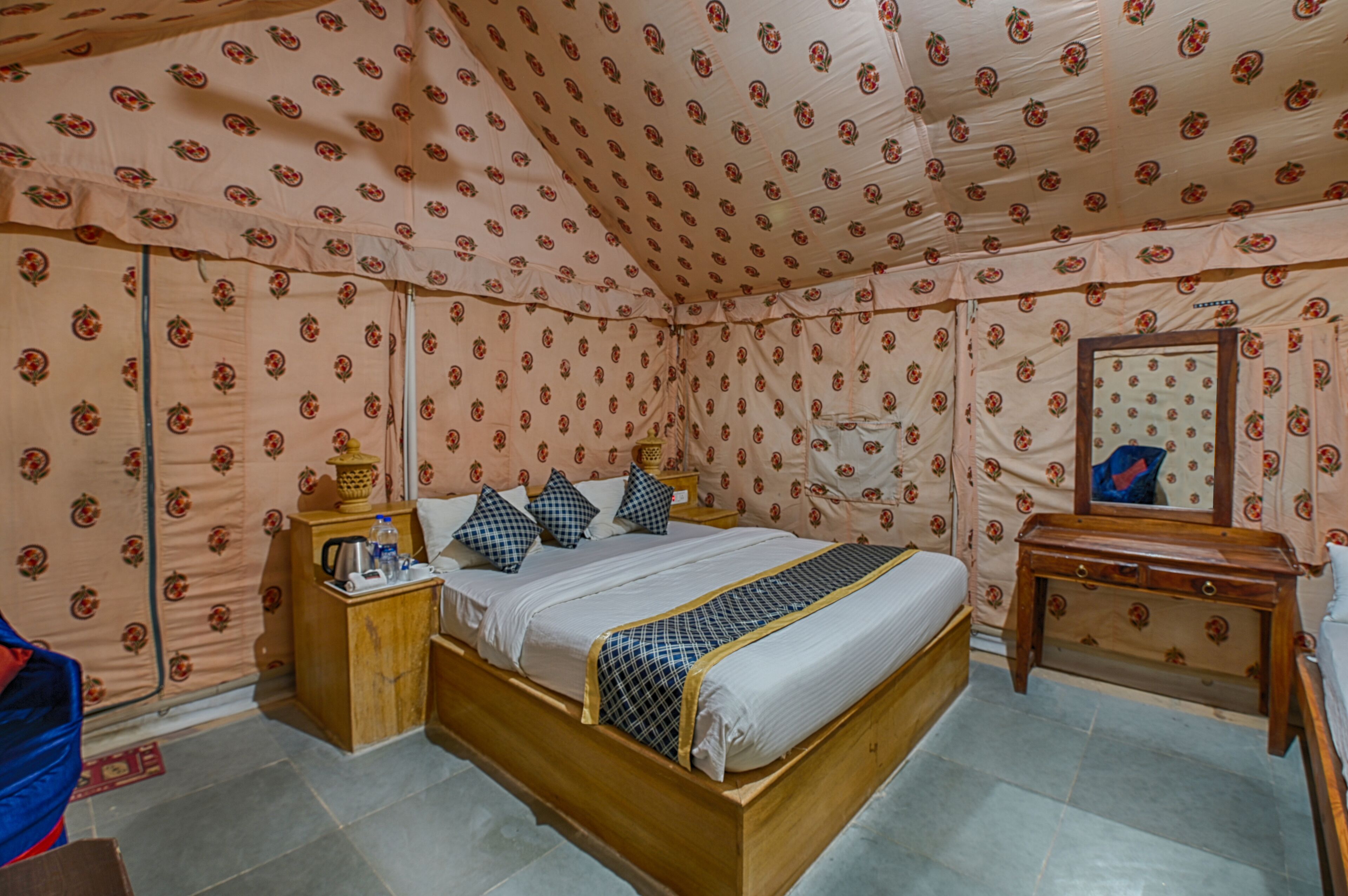A room with a bed, a wooden nightstand, a small table, and a mirror.