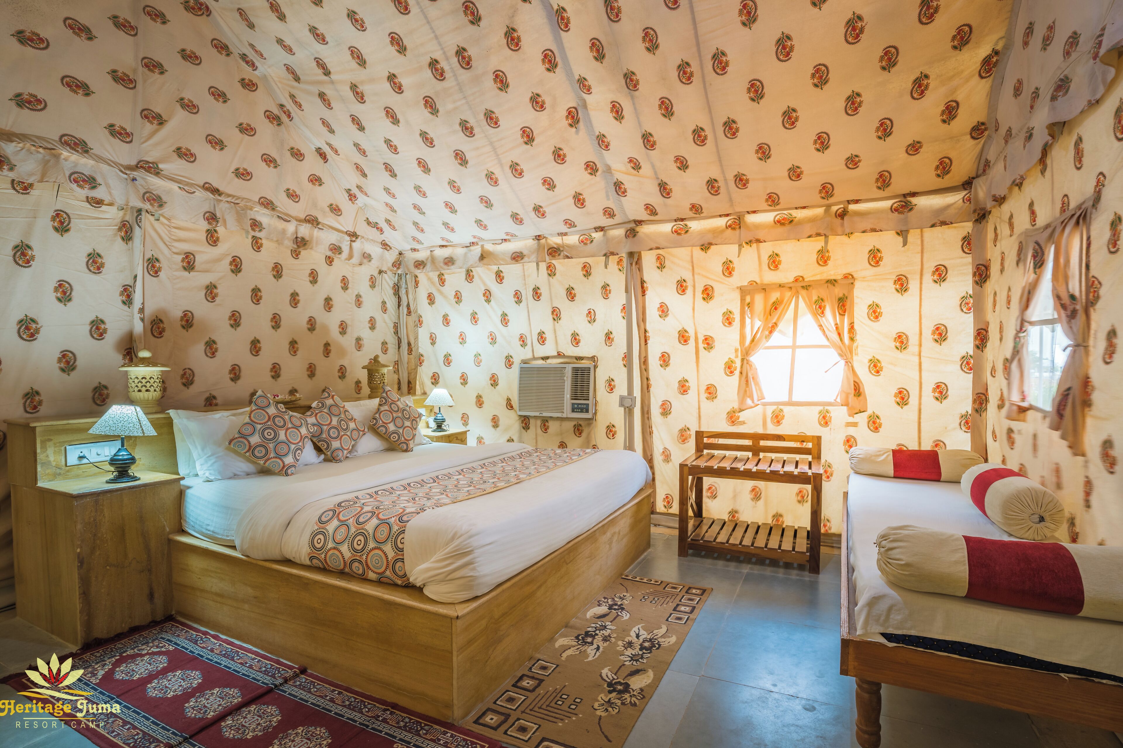 A cozy, well-lit bedroom with a large bed, a bedside table with a lamp, and a small wooden chair.