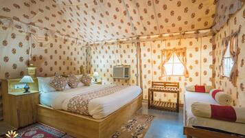 A cozy, well-lit bedroom with a large bed, a bedside table with a lamp, and a small wooden chair.