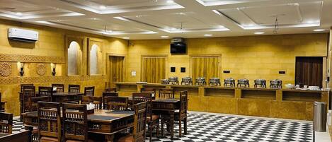 A hotel lobby with a checkered floor, wooden tables and chairs, a buffet area, and recessed lighting.