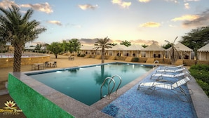 A resort pool with lounge chairs, palm trees, and a clear sky. - Heritage Juma Resort Camp (Jaisalmer)