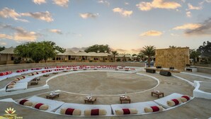 Un espacio de estar al aire libre circular con cojines blancos y rojos, mesas y una estructura decorativa central.