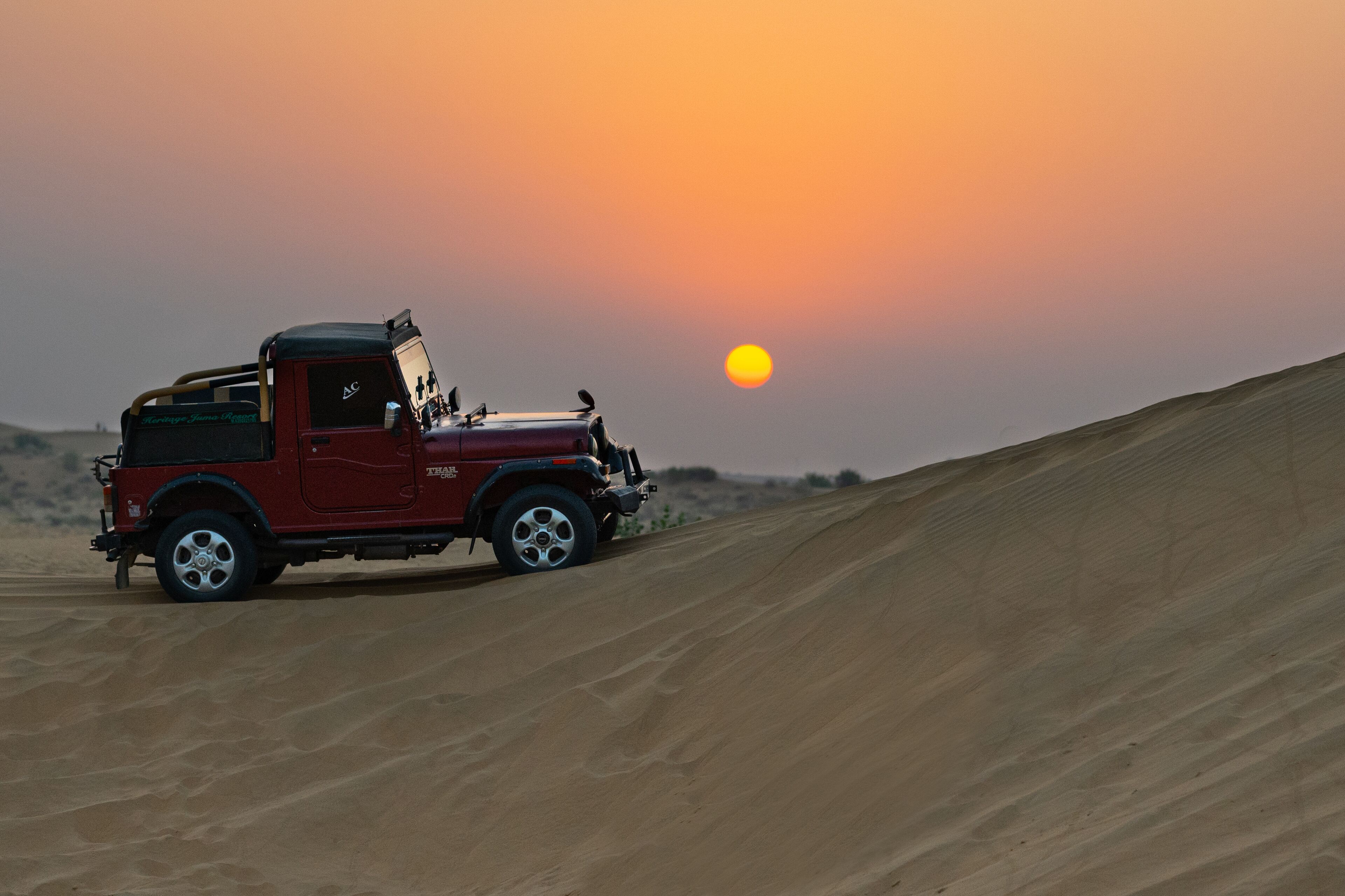 A red off-road vehicle on a sandy dune at sunset.