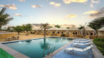 A resort pool with lounge chairs, palm trees, and a clear sky.