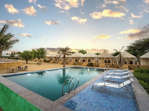 Piscina de resort con sillas de descanso, palmeras y cielo despejado.