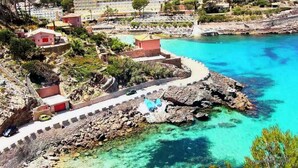 Eine Küstenlandschaft mit klarem türkisblauem Wasser, einer felsigen Uferlinie und einem gepflasterten Weg.
