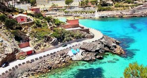 Una zona costera con aguas turquesas cristalinas, un litoral rocoso y un camino pavimentado.