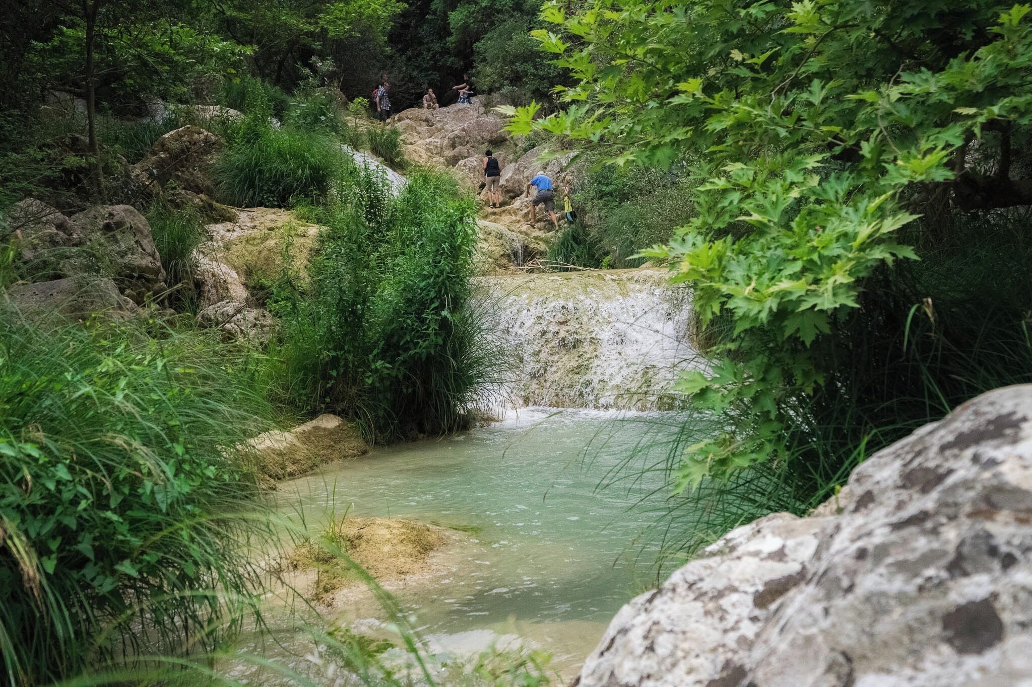 Un cadre naturel en plein air, agrémenté d’une petite cascade, entourée de rochers et de verdure.