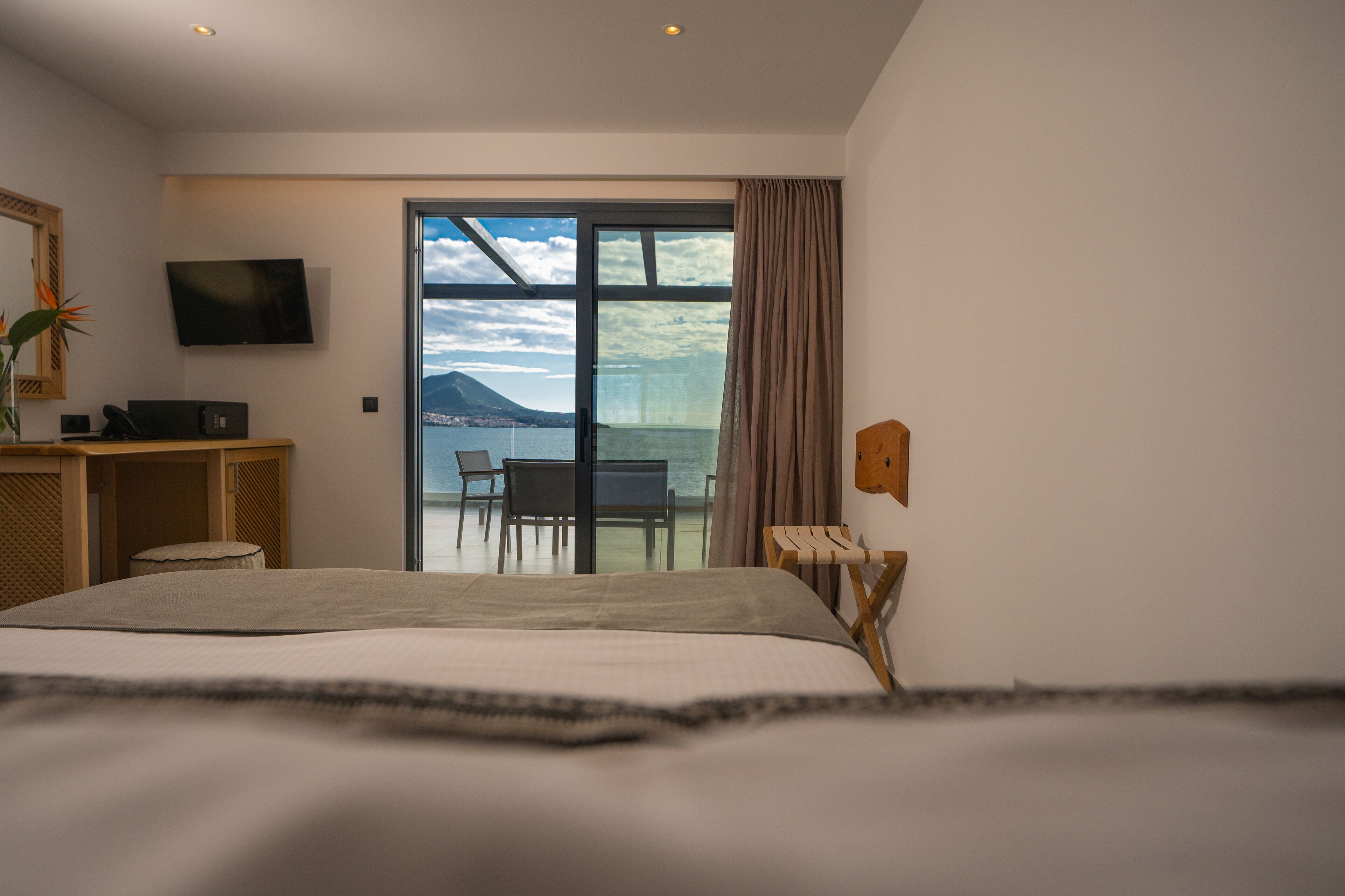 A hotel room with a bed, a desk, a chair, a TV, and a view of the sea.