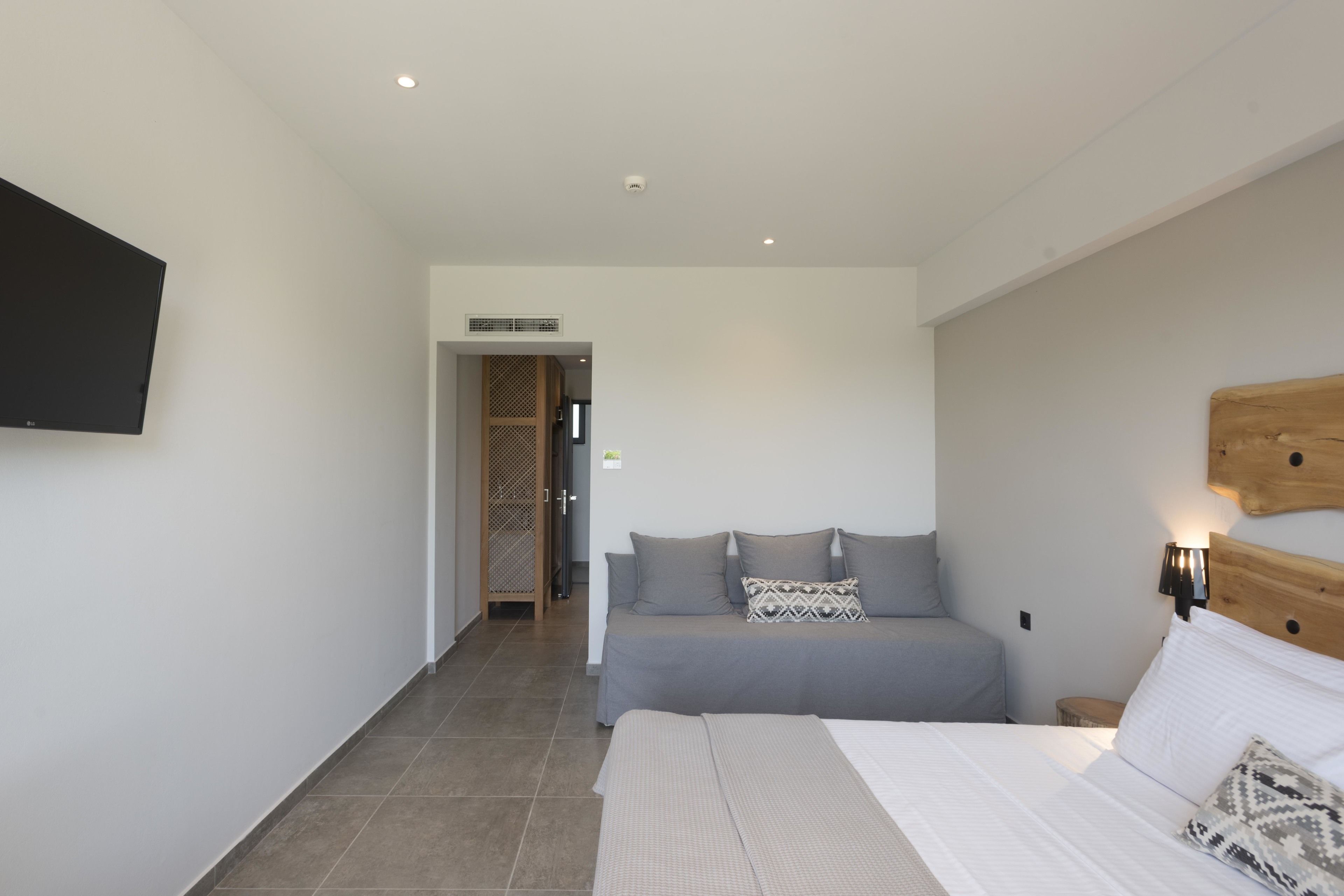 A modern bedroom with a large bed, a flat-screen TV mounted on the wall, and a wooden headboard.